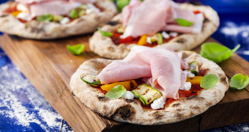 Personal pizzas with cooked ham, grilled vegetables and caprino cheese  